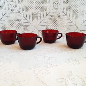 May include: Set of four ruby red glass cups with handles. The cups are on a white lace tablecloth.