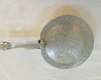 May include: A silver aluminum serving tray with a floral design. The tray has a handle and is embossed with a flower and leaves.