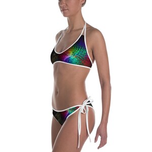 Pode incluir: Um conjunto de biquíni de duas peças com um design vibrante e colorido. O top halter e a parte de baixo apresentam um padrão de azuis, verdes, vermelhos e amarelos brilhantes sobre um fundo preto. A borda branca contorna as bordas do biquíni.