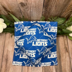 May include: A blue and white fabric square pillow with the Detroit Lions logo repeated on the front. The pillow is made of a soft, comfortable fabric and is perfect for adding a touch of team spirit to any room.