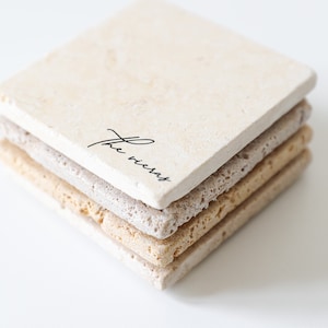 May include: A stack of four square beige coasters with a slightly rough texture. The top coaster has the words "the viceroy" written in black cursive.