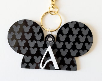 May include: Black and white Mickey Mouse ears keychain with a white letter A in the center. The keychain has a gold split ring and a gold lobster clasp.