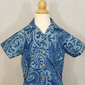 Puede incluir: Una camisa azul de manga corta con un dise&ntilde;o estampado en blanco y azul. La camisa tiene cuello y botones.