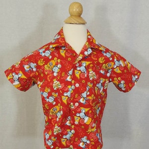 May include: Red short-sleeved button-up shirt with a colorful print of cartoon mice playing musical instruments. The shirt has a collar and a button-up front.