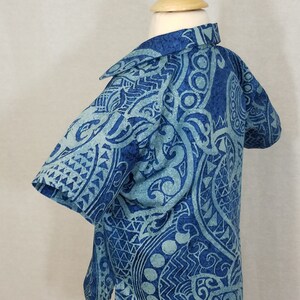 Puede incluir: Una camisa de manga corta azul y blanca con estampado y cuello. La camisa tiene un dise&ntilde;o tradicional polinesio.
