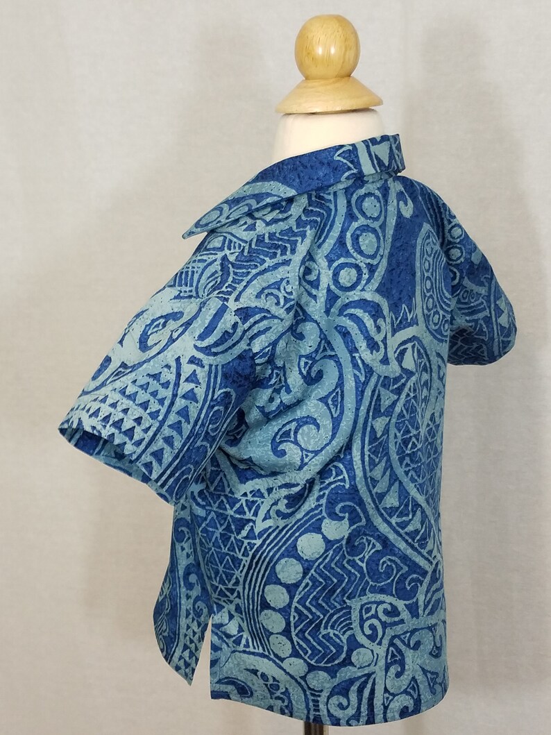 Puede incluir: Una camisa de manga corta azul y blanca con estampado y cuello. La camisa tiene un dise&ntilde;o tradicional polinesio.