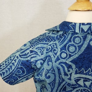 Puede incluir: Una camisa azul de manga corta con un dise&ntilde;o estampado que presenta formas abstractas y remolinos. La camisa tiene cuello y cierre de botones en la parte delantera.