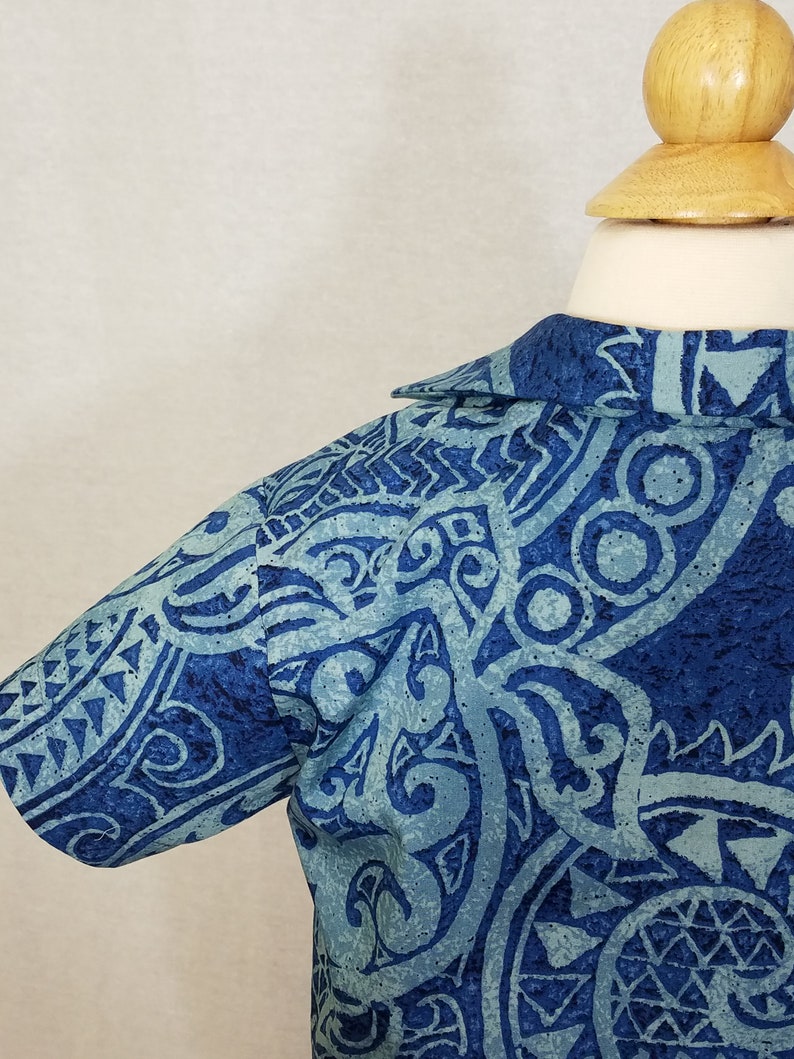 Puede incluir: Una camisa azul de manga corta con un dise&ntilde;o estampado que presenta formas abstractas y remolinos. La camisa tiene cuello y cierre de botones en la parte delantera.