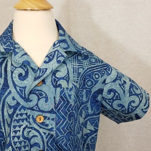 Puede incluir: Una camisa de manga corta con cuello abotonado y un estampado azul y blanco. La camisa tiene un dise&ntilde;o geom&eacute;trico con fondo azul y detalles blancos.