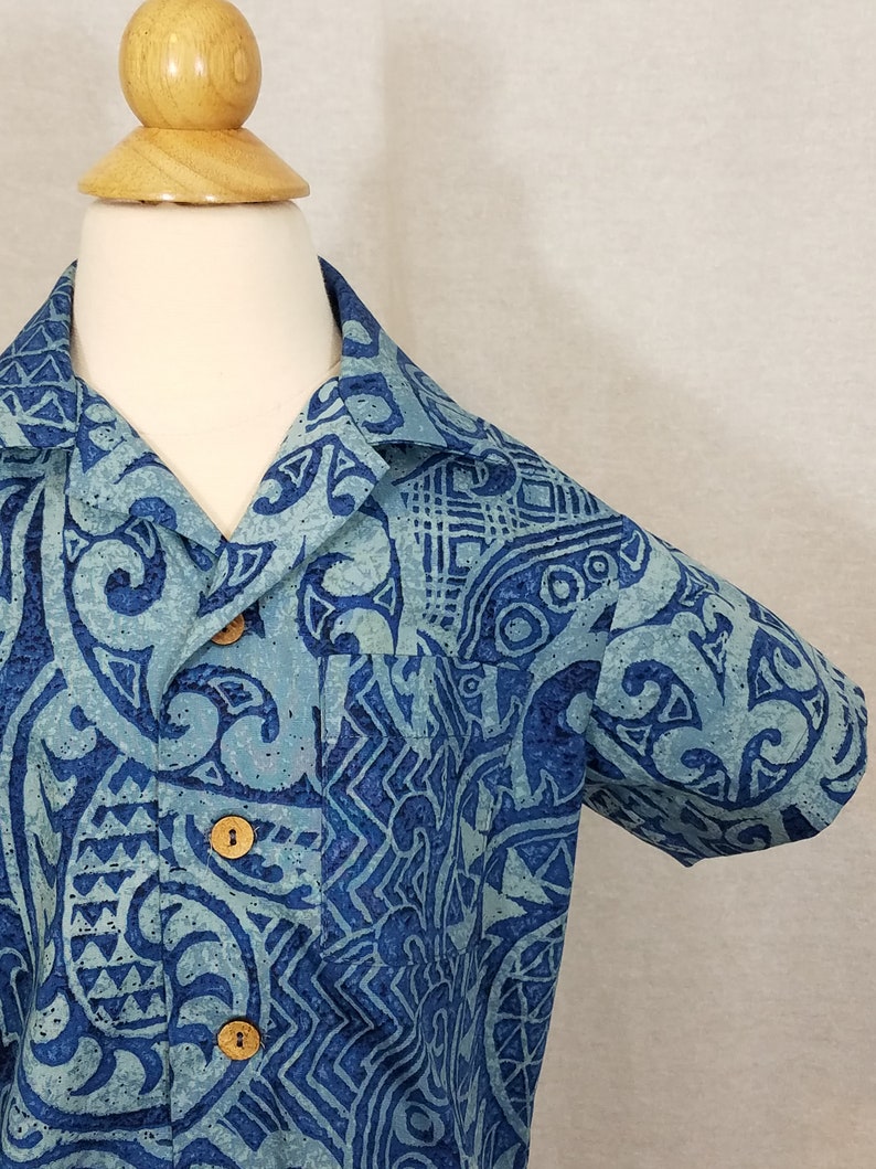 Puede incluir: Una camisa de manga corta con cuello abotonado y un estampado azul y blanco. La camisa tiene un dise&ntilde;o geom&eacute;trico con fondo azul y detalles blancos.