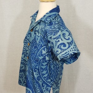 Puede incluir: Una camisa azul de manga corta con un dise&ntilde;o estampado en blanco y azul. La camisa tiene un cuello abotonado y un solo bot&oacute;n en la parte delantera.
