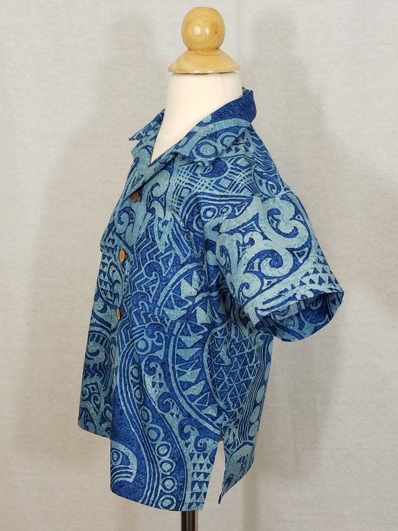 Puede incluir: Una camisa azul de manga corta con un dise&ntilde;o estampado en blanco y azul. La camisa tiene un cuello abotonado y un solo bot&oacute;n en la parte delantera.