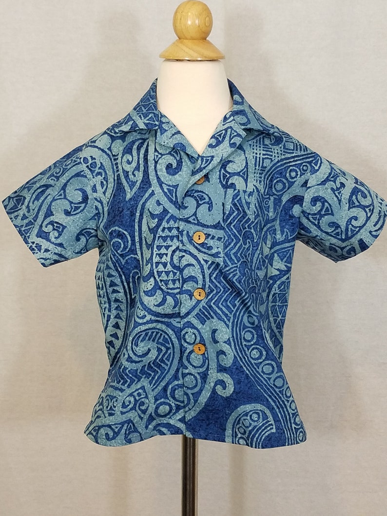 Puede incluir: Una camisa azul de manga corta con un dise&ntilde;o estampado en blanco y azul. La camisa tiene cuello y botones.
