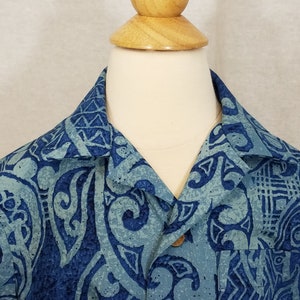 Puede incluir: Una camisa de manga corta con estampado azul y verde con cierre de botones de madera. La camisa tiene un dise&ntilde;o tradicional hawaiano.