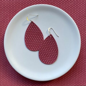 May include: A pair of teardrop-shaped earrings with a textured honeycomb pattern. The earrings are made of dark burgundy leather and have silver hooks.