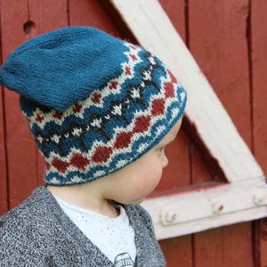 May include: A child wearing a blue and red patterned knit hat. The hat has a blue brim and a red and white geometric pattern.