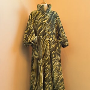 May include: A long, green and cream patterned coat with a high collar and button closure. The coat has a flowing, loose fit and is made of a soft, plush fabric.