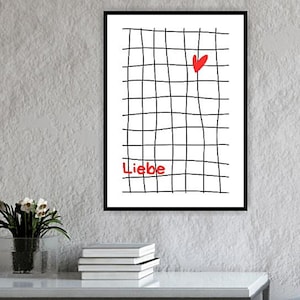 May include: A framed art print with a black grid design, a red heart, and the word "Liebe" in red. The artwork hangs on a white wall above a white table with books and a dark grey ottoman.
