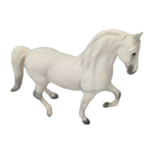 May include: A white horse figurine standing in a dynamic pose with one front leg lifted. The horse features a long, flowing mane, a tail with grey shading at the tip, and grey-toned hooves. The sculpture is rendered in a matte finish.