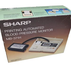 May include: A vintage Sharp Printing Automated Blood Pressure Monitor, model MB-371H, in its original box. The box is tan and green with product details and diagrams. The monitor itself is off-white with a black cuff and tubing.