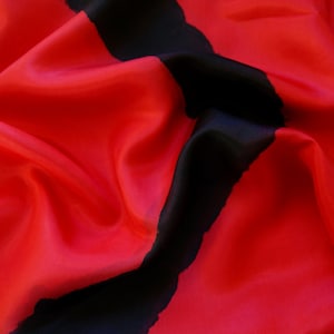 Könnte beinhalten: Ein rotes Seidentuch mit einem auffälligen, unregelmäßigen schwarzen Streifen. Der Stoff ist drapiert, wodurch seine fließende Textur und sein Glanz zur Geltung kommen. Ein farbenfrohes Accessoire für verschiedene Anlässe.