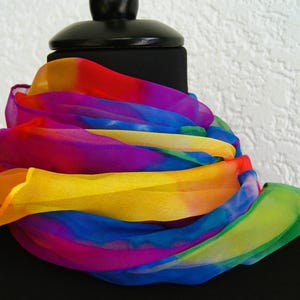 Könnte beinhalten: Ein mehrfarbiger Schal, drapiert über einem schwarzen Mannequinkopf. Der Schal zeigt ein Regenbogenspektrum an Farben, darunter Rot, Gelb, Blau, Grün und Lila. Der transparente Stoff ist in fließenden Falten angeordnet.