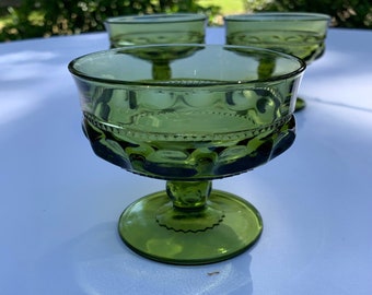 May include: Three green glass dessert dishes with a scalloped rim and a textured base. The dishes are on a white tablecloth.