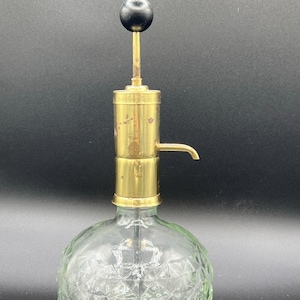 May include: A vintage perfume bottle with a clear, diamond-patterned glass base and a brass pump. The pump has a black ball on top. The bottle is designed to dispense liquids and has a small spout.