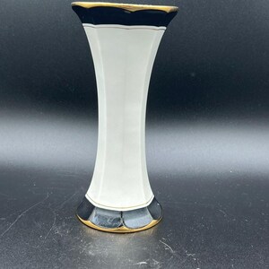 May include: A white ceramic vase with a flared top and base, featuring dark navy blue bands at the rim and bottom. The edges of the navy blue sections are accented with a thin gold trim, and the body of the vase has a vertical, paneled design.
