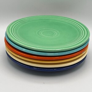 May include: A stack of six colorful ceramic plates. The plates are in shades of green, blue, orange, yellow, and blue. The plates are stacked in a rainbow pattern.