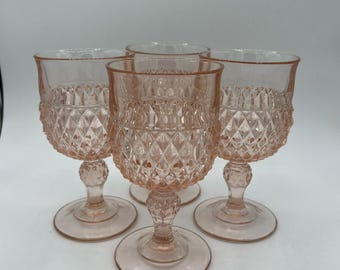 May include: Four pink-tinted vintage wine glasses. Each glass features a diamond pattern on the bowl, a round base, and a decorative stem. The glasses are made of glass and are displayed against a white background.