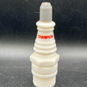 May include: A white Champion spark plug with a gray top and red lettering. The spark plug has a ridged design and a hexagonal base. The product is a collectible or decorative item.