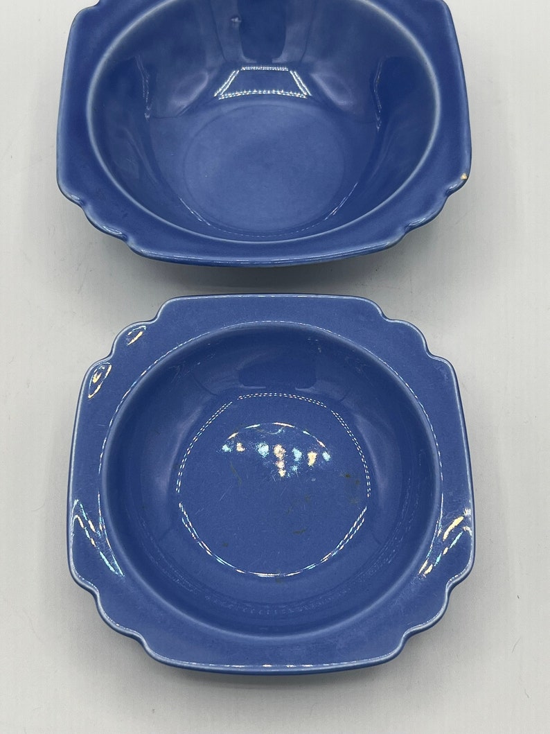 May include: Two blue ceramic bowls with square rims and a slightly rounded bottom. The bowls are a deep blue color and have a glossy finish.