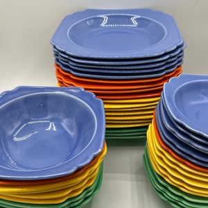 May include: A stack of blue, orange, yellow, and green ceramic bowls. The bowls have a scalloped edge and are stacked in a rainbow pattern.