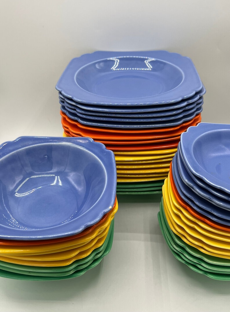 May include: A stack of blue, orange, yellow, and green ceramic bowls. The bowls have a scalloped edge and are stacked in a rainbow pattern.