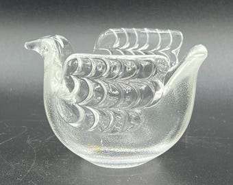 May include: Clear glass bird-shaped decorative bowl. The bowl features a detailed design with textured wings and tail feathers. The bird has a curved beak and a rounded body, perfect for holding small items or as a decorative piece.