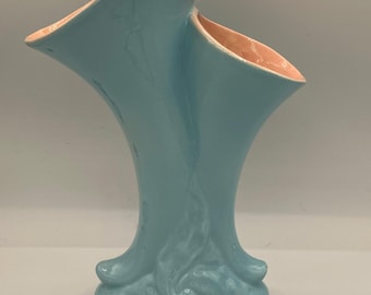 以下が含まれることがあります： ユニークな非対称デザインの、水色のセラミック花瓶。花瓶は、内側がピーチ色のフレアトップです。ベースは、様式化された有機的な形状をしています。この装飾的な花瓶は、花を飾ったり、単独のアート作品として飾るのに適しています。