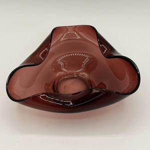 May include: A vintage, amethyst-colored glass bowl with a unique, ruffled rim. The bowl has a smooth, glossy finish and a deep, rounded shape. The dark purple color is consistent throughout the glass, creating a striking visual effect. This decorative bowl is ideal for display.