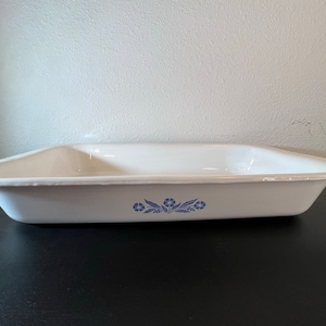 May include: White ceramic baking dish with a blue floral design. The dish is rectangular and has a slightly rounded bottom.