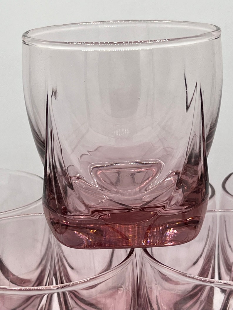 May include: Set of six clear glass tumblers with a pink hue and a unique, faceted design. The glasses are stacked on top of each other.