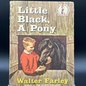 May include: A hardcover book titled Little Black, A Pony by Walter Farley. The cover features an illustration of a child in a red sweater feeding a black pony through a wooden stable door. The top right corner displays the Beginner Books logo.