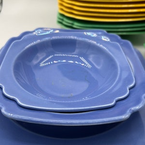 May include: Two blue ceramic plates, one a shallow bowl with a scalloped edge, stacked on top of a larger square plate.