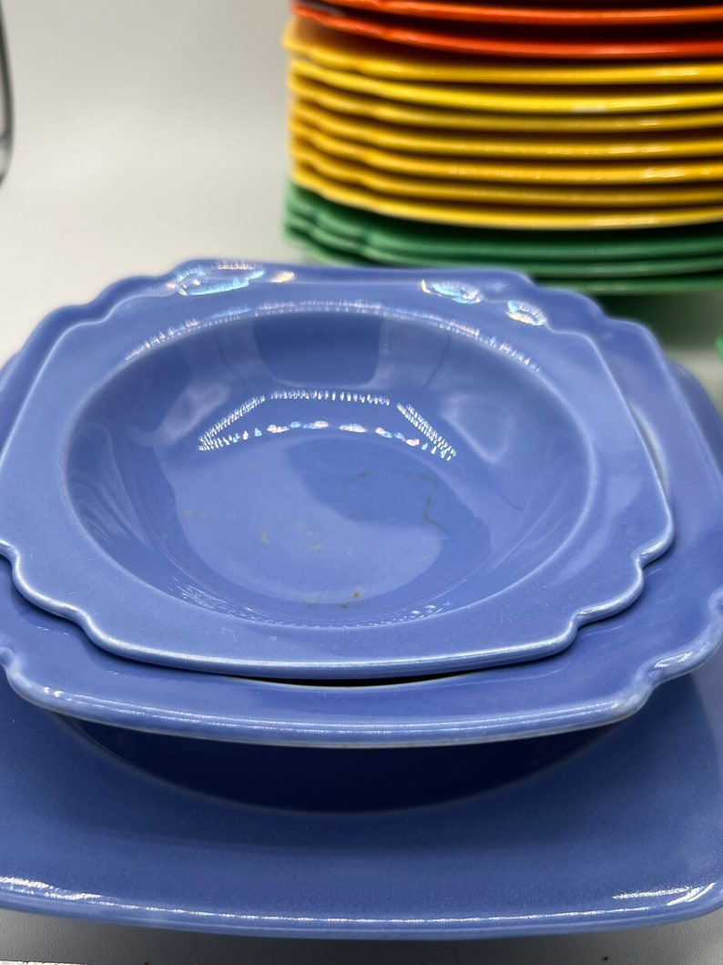 May include: Two blue ceramic plates, one a shallow bowl with a scalloped edge, stacked on top of a larger square plate.