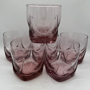 May include: Set of six clear glass tumblers with a pink hue and a square shape. The glasses have a decorative design with a wavy pattern.