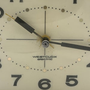 May include: A white analog clock face with black numbers and hands. The clock face has a black Westclox Electric logo and the text "Made in U.S.A."