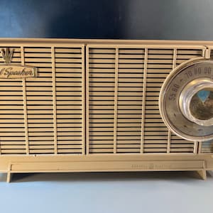 May include: A vintage beige and gold AM radio with a dial that reads "55 60 70 80 90 100 140 160" and a "Dual Speaker" label.