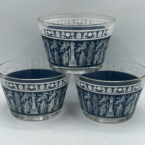 May include: Three clear glass bowls with a navy blue band featuring a white Greek key design and figures. The bowls are stacked, showcasing the detailed artwork around the rim. The bowls are likely for serving or display.
