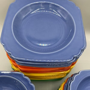 May include: A stack of blue square-shaped ceramic bowls with scalloped edges. The bowls are stacked in a rainbow pattern with orange, yellow, and green.