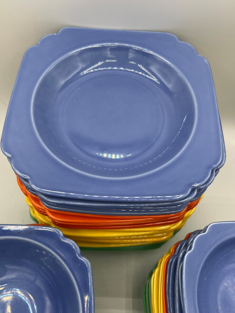 May include: A stack of blue square-shaped ceramic bowls with scalloped edges. The bowls are stacked in a rainbow pattern with orange, yellow, and green.