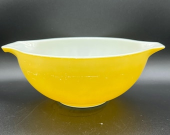 May include: A vintage yellow mixing bowl with a white interior. The bowl has a rounded shape with two small handles on either side. The bowl is made of glass and has a glossy finish.